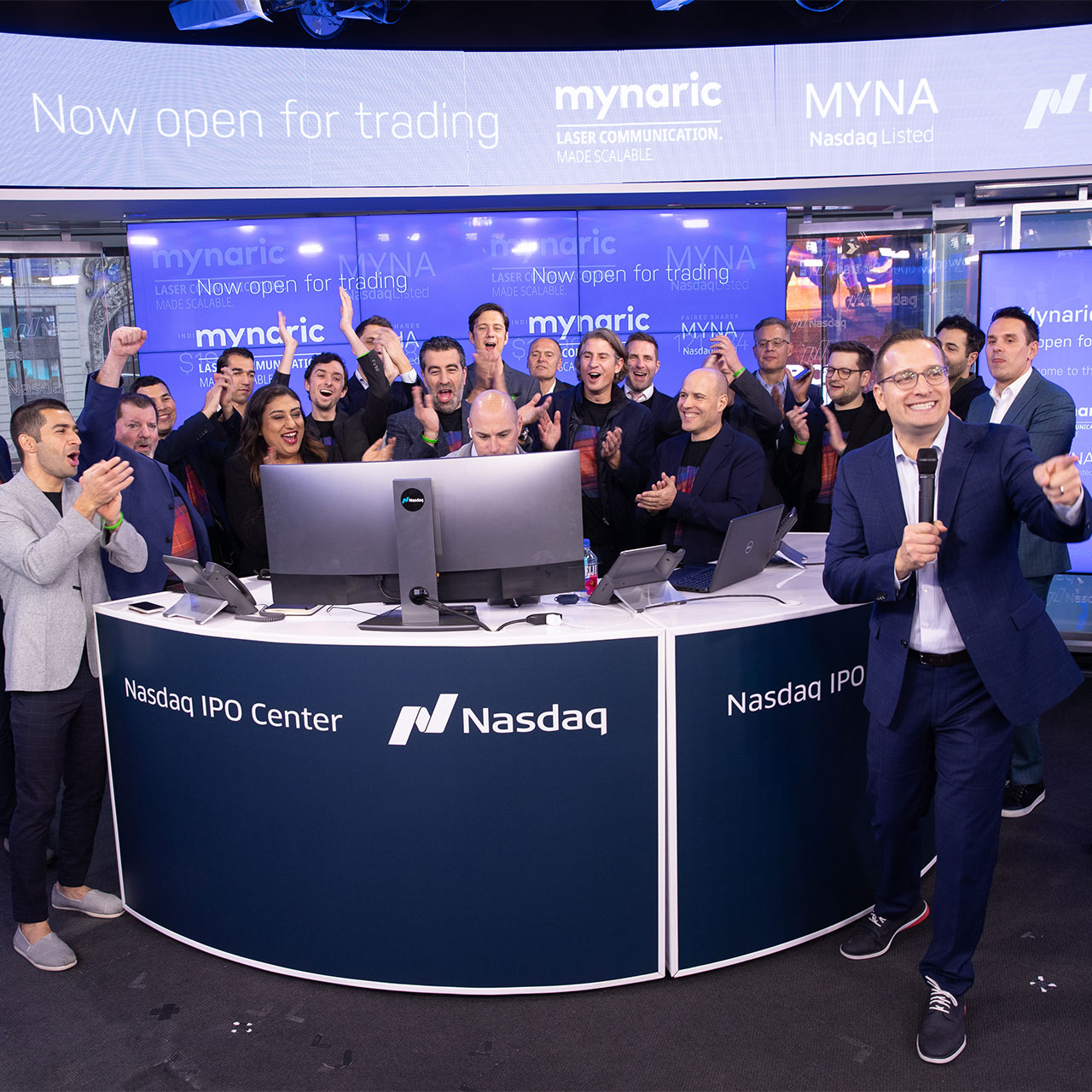 Gruppenfoto des Mynaric Teams, während sie lachen und klatschen am Tag des Börsengangs. Sie stehen im Nasdaq IPO Center.